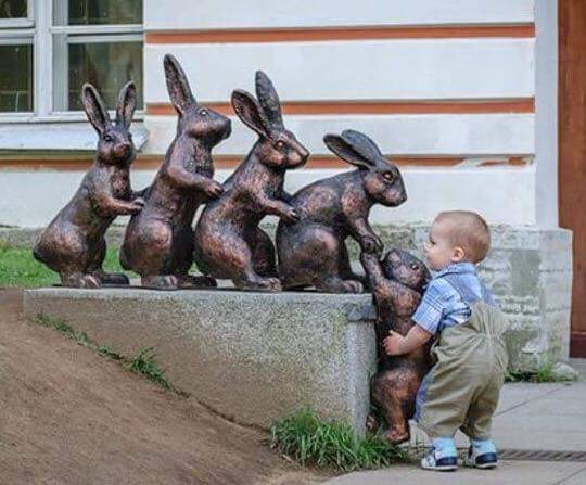 Bebé trata de ayudar a un conejo de piedra (estatua de varios conejos en fila) - Empatía infantil